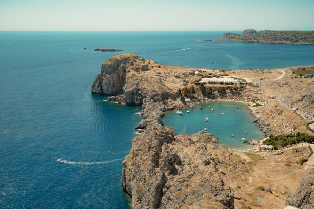 Lindos Bay: This image shows the bay surrounded by rocky cliffs and hills. The crystal-clear water in the bay is filled with anchored boats, adding dynamic elements to this serene setting.