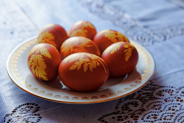 istock The image shows seven brown eggs with yellow leaf patterns on a white plate with a gold rim, placed on a blue and white lace tablecloth. 2155316151