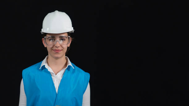 istock The young engineer posed for the camera wearing her work clothes, helmet and safety glasses. Beautiful woman working in construction in front of black background wearing blue work vest, white helmet and safety glasses. 2155317523