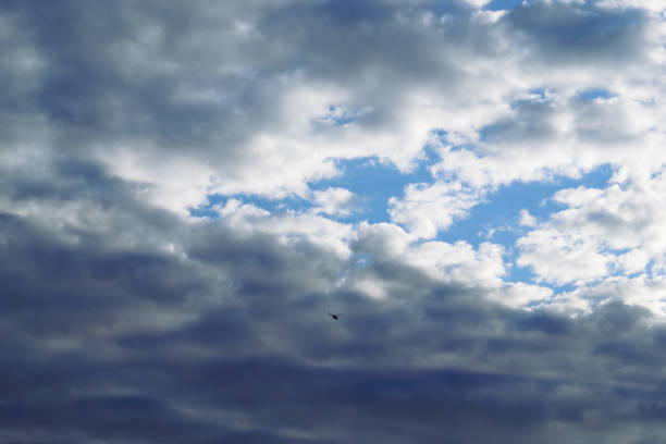 The helicopter is flying high in the sky against the background of cumulus clouds