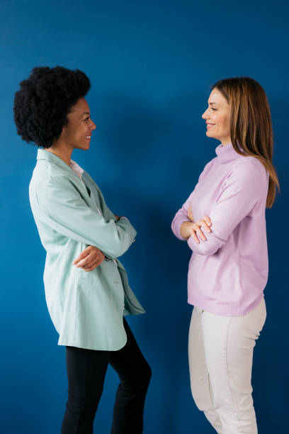 Two young businesswomen standing face to face on blue background
