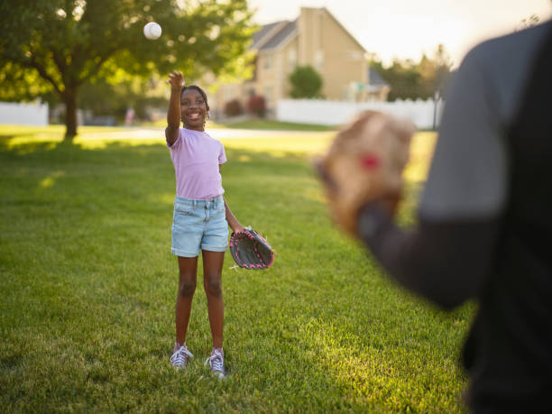 A grandfather and granddaughter spending time together in a park practicing baseball.