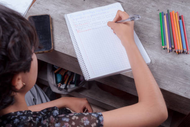 istock Hands of a young woman doing homework, she writes in her notebook, homework topic. 2155343290
