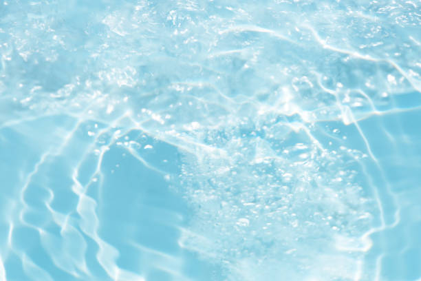Blue water with ripples on the surface. Defocus blurred transparent blue colored clear calm water surface texture with splashes and bubbles. Water waves with shining pattern texture background.