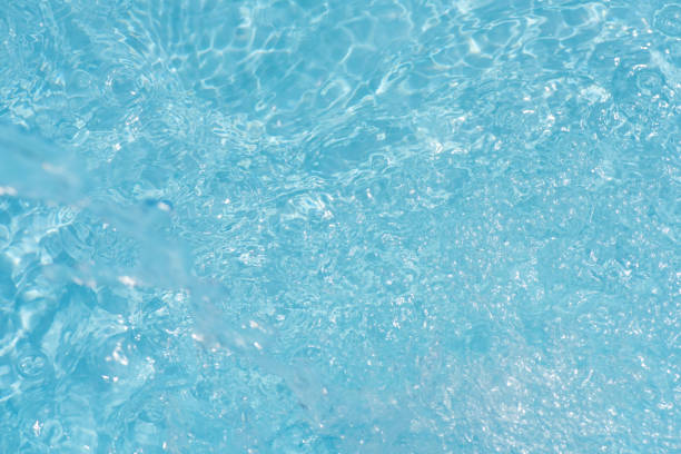 Blue water with ripples on the surface. Defocus blurred transparent blue colored clear calm water surface texture with splashes and bubbles. Water waves with shining pattern texture background.