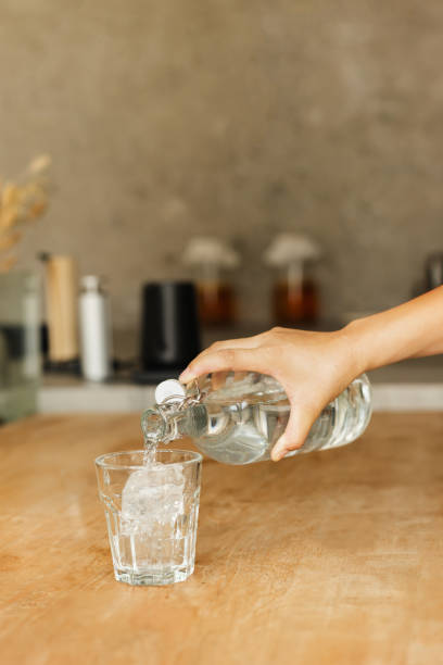 istock Hand pouring fresh purified water from a bottle into a glass in vertical. 2155364096