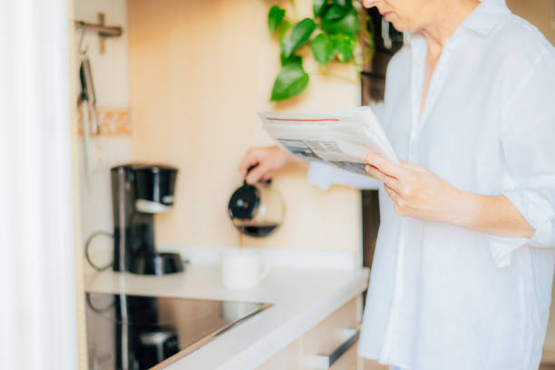 istock Person Pouring Fresh Coffee Into A Mug While Reading A Newspaper In The Kitchen. 2155376225