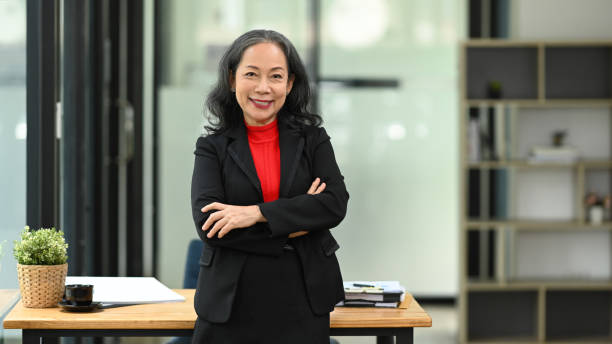 istock Confident mature businesswoman with financial document standing at workplace 2155383408