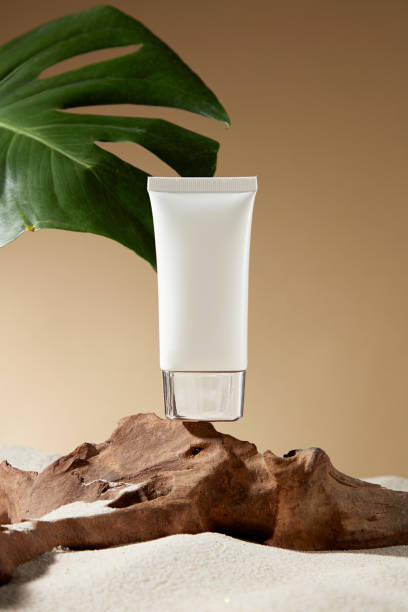 istock A rugged stone pedestal placed on the fine white sand displays a blank label white cosmetic tube on top, behind a brown background and a green monstera leaf for decoration. Cosmetic advertising photo 2155391087