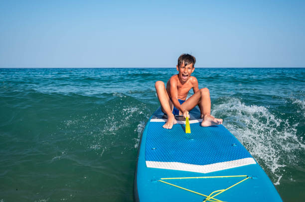 happy boy sitting on a surfboard in the sea on the waves is scared and playing