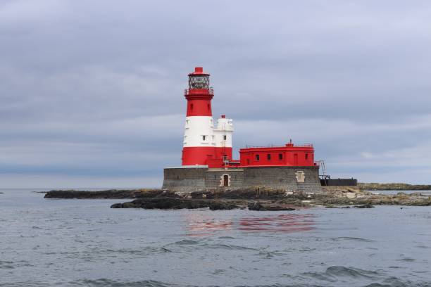 istock Red and white striped lighthouse on a rocky island surrounded by sea 2155396489