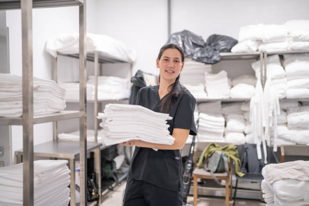 istock Mid adult maid packing bed sheets on shelf in hotel laundry 2155397602