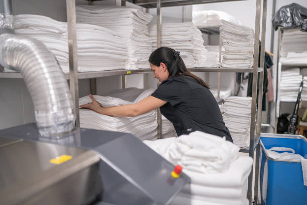 istock Mid adult maid packing bed sheets on shelf in hotel laundry 2155397757
