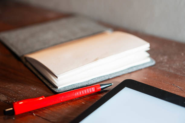 istock Red pen, open notebook, and tablet on wooden surface 2155399722
