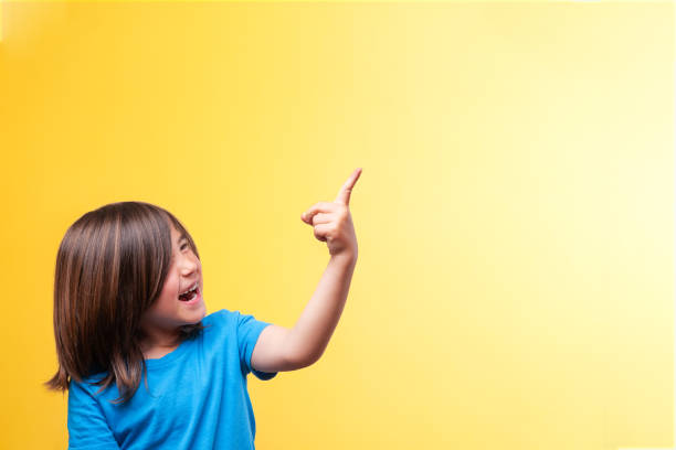 istock Smiling boy pointing to space for text. Blue t-shirt. Yellow background. Emotions. 2155408607