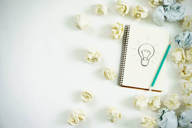a notebook with a drawn bulb on it, a pencil and paper balls of a new window