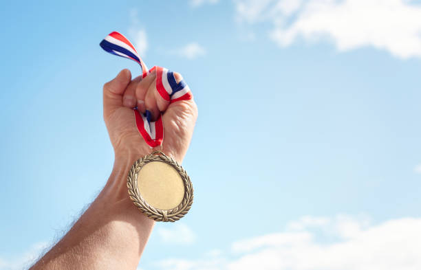 istock Gold medal held in athlete hand raised against sky background 2155413328