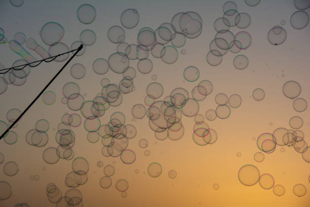 Lots of colorful soap bubbles floating in the orange sky at sunset with soap bubble stick