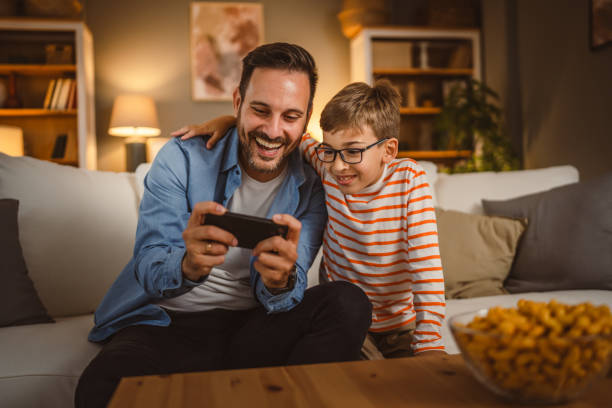 istock Father and son sit on sofa and use mobile phone at home have fun 2155427928