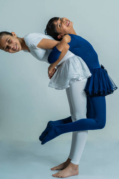 Latin sisters of average age of 10 and 12 years old dressed in ballet uniform are in a photo studio performing their ballerina poses while being photographed