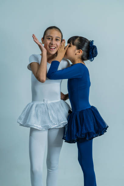 Latin sisters of average age of 10 and 12 years old dressed in ballet uniform are in a photo studio performing their ballerina poses while being photographed