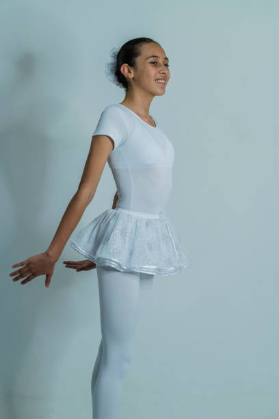 Latin girl of average age of 10 years old dressed in a ballet uniform is in a photo studio performing her ballerina poses while being photographed