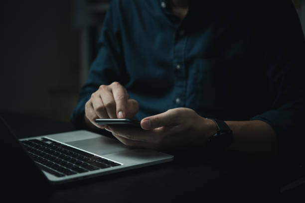 istock A man is using his cell phone while sitting at a desk with a laptop 2155437488