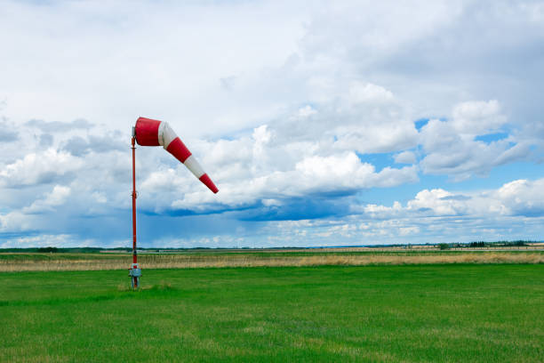 Striped red and white weather vane flies in wind in the airfield with green grass and the background with dark blue cloudy sky before storm.