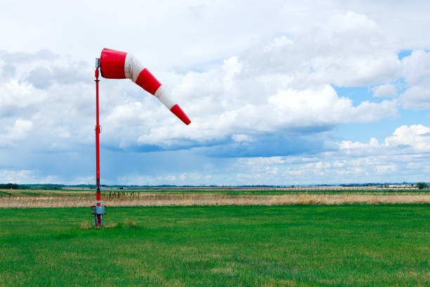 Striped red and white weather vane flies in wind in the airfield with green grass and the background with dark blue cloudy sky before storm.