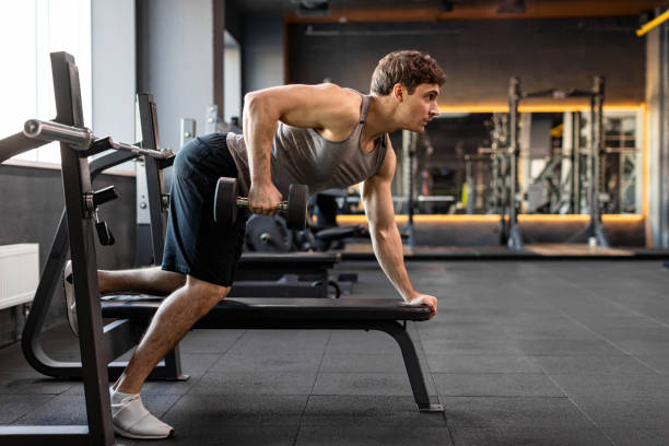 istock Muscular bodybuilder man doing exercises with weights, lifting dumbbells at bench in gym interior, side view, free space 2155448103