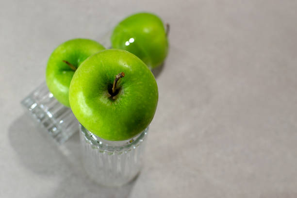 Three green apples and two overturned (upside down) transparent crystal glasses.