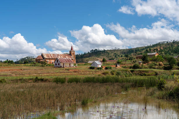 Village close to the Ambositra with small church and some mud houses, rice fields and small pond with fishes. Rural landscape and blue sky. Close to Ambositra, Madagascar.