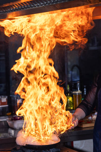 Chef creates flame in pan. Chef cooking with flame in a frying pan on a kitchen stove. Young chef in the restaurant kitchen making flambe in the frying.