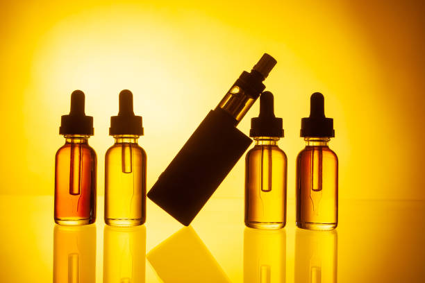 istock Electronic cigarette and liquid on yellow background. Selling VAPE. Vaping accessories. Gadgets for vaper. Smoking electronic cigarettes. Smoking liquid. Replacing conventional cigarettes. 2155464839