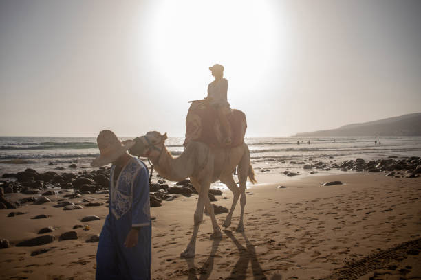 istock Young woman rides camel with guide 2155465827