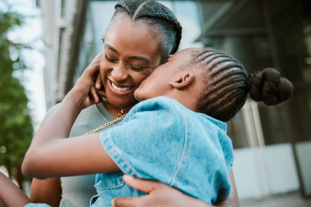 Daughter Kisses Her Mother A Black mother and her girl snuggle playfully, the mom holding her daughter and the girl kissing her on the cheek. Shot in Houston, Texas. black mother and adult daughter stock pictures, royalty-free photos & images