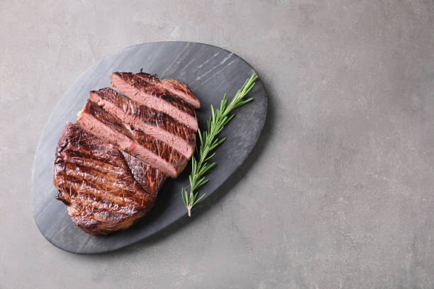istock Delicious fried beef meat with rosemary on grey textured table, top view. Space for text 2155473403