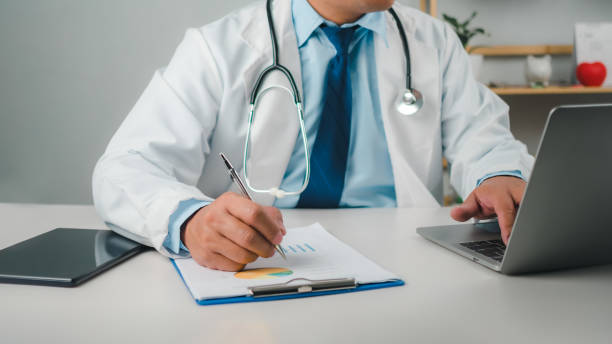 istock Male doctor sitting at work desk checking work plans and writing document reports in hospital office, healthcare worker and doctor service, digital laptop in modern office, medical technology concept. 2155473743