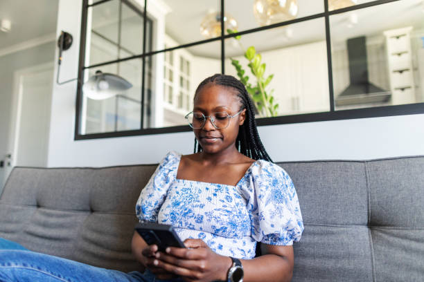 istock Young adult woman using mobile at home sitting on sofa 2155476787
