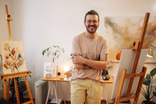 Young artistic painter smiling at camera with arms crossed at atelier