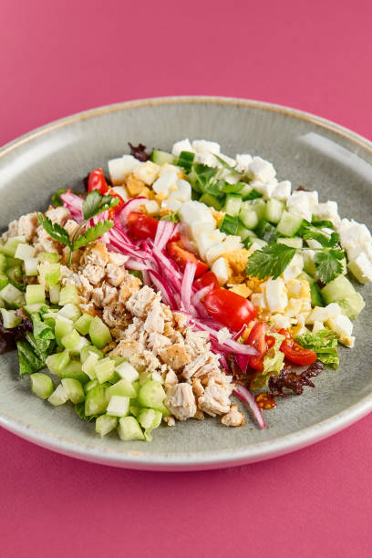 istock Fresh Cobb Salad with Mixed Greens, Chicken, Tomato, and Crumbled Cheese on Pink Background 2155482148