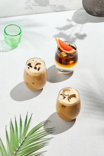 istock Assorted iced coffee on white concrete background with palm shadows. Minimal composition with cold summer drinks: espresso tonic, ice moccachino and latte. Summer composition for coffee menu. 2155482183