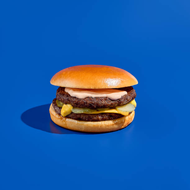 istock Massive double-patty burger on a blue background, boasting juicy meat and bold flavors. Modern minimalist food photography captures this irresistible and indulgent fast food treat. Square shot. 2155482208