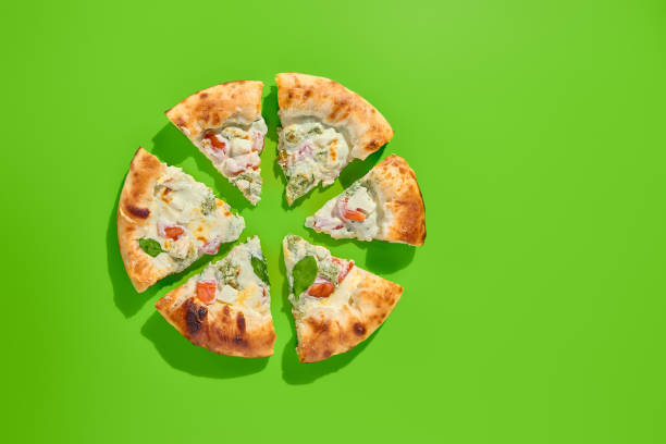 istock Sliced four cheese pizza with tomatoes and spinach on a bright green background, top view. Minimalist style, perfect for modern food photography, takeout, or casual meal. Fresh spinach leaves 2155482240