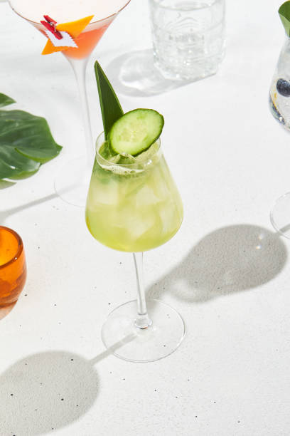 istock Cucumber cocktail in wine glass on white concrete background with shadows. Fresh mocktail in minimal style with tropical leaves. Alcoholic drink with gin and cucumber on summer menu. Summer drink. 2155482282