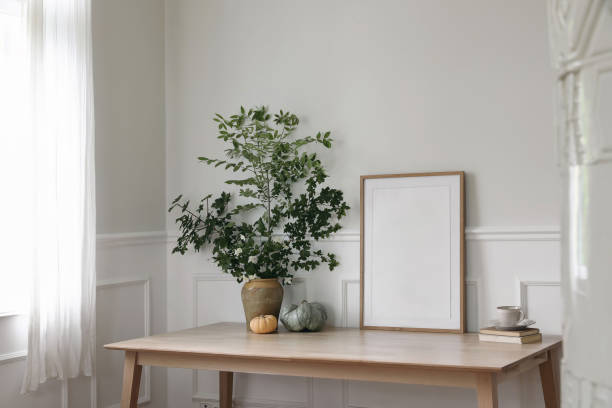 istock Home office concept. Old books, empty vertical wooden picture frame mockup on office desk, table. Tree branches in vase. Cup of coffee, pumpkins. Working space. Scandinavian interior. Blurred stove 2155484893