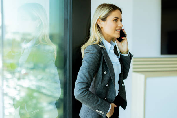 istock Smiling businesswoman talking on mobile phone by office window in daylight 2155484936