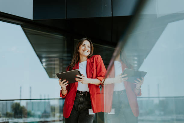 istock Smiling businesswoman in red blazer using tablet at modern office window in daylight 2155484957