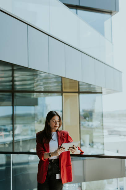 istock Smiling businesswoman in red blazer using tablet at modern office window in daylight 2155484977