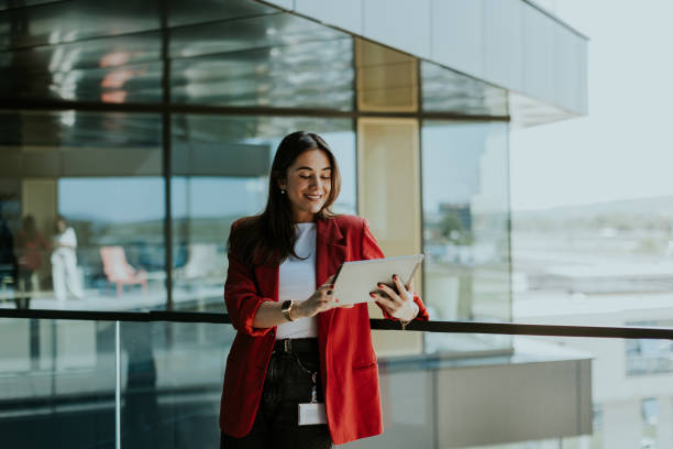 istock Smiling businesswoman in red blazer using tablet at modern office window in daylight 2155484992